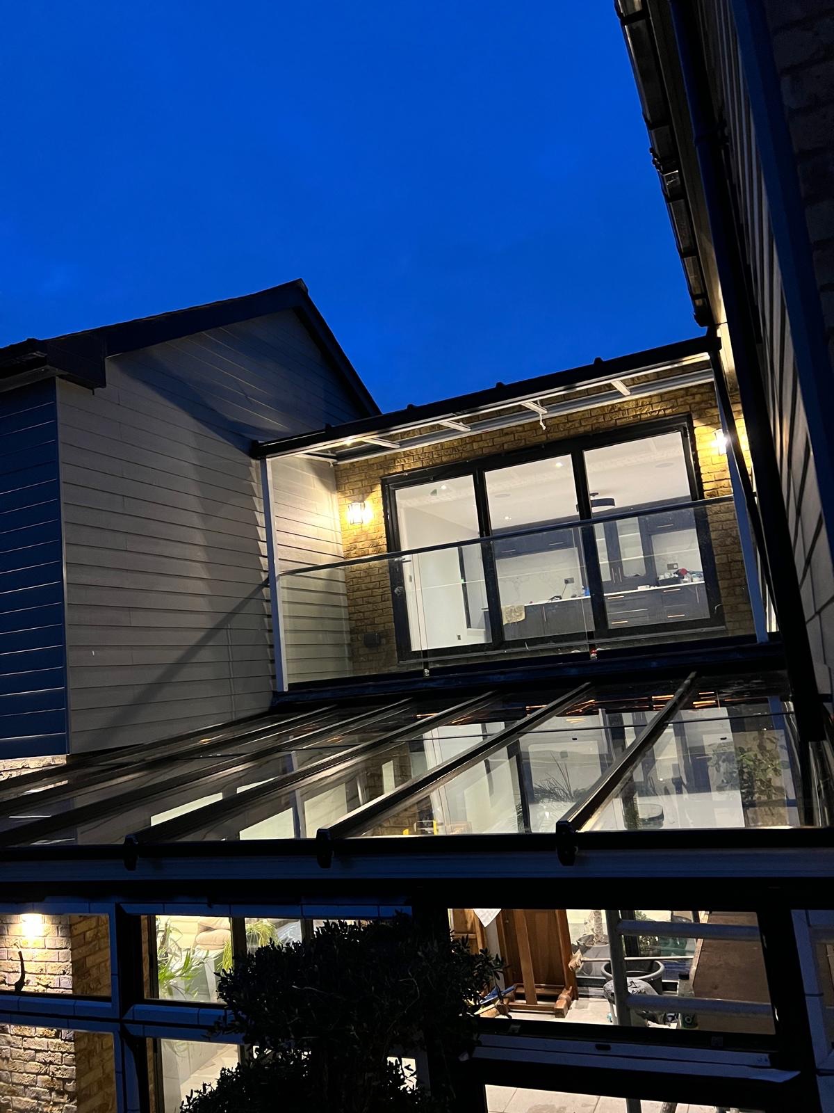 Twilight rear view of a London home with new bi-fold doors and glass conservatory roof installed by Ertan Glass